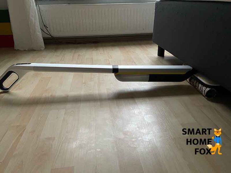 Man sieht, wie mit dem Kärcher FC 7 cordless Premium unter einem Sofa gereinigt wird.